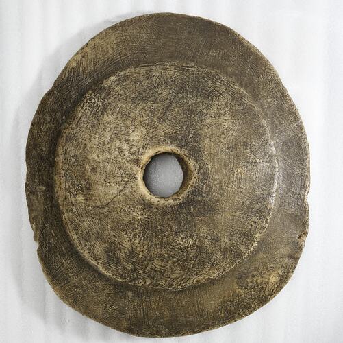 Round irregular brown stone disc with central hole.