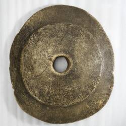 Round irregular brown stone disc with central hole.