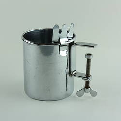 Metal beaker with screw attachment at side.