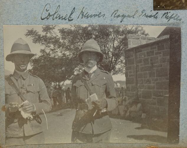 Two men in military uniform standing near a stone wall.