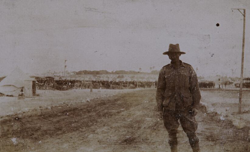 Soldier with Vehicles and Camp in Background