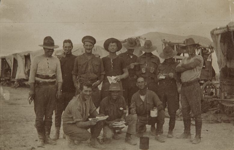 Eight soldiers stand in a line, three squat in front. Six men hold letters or photographs.