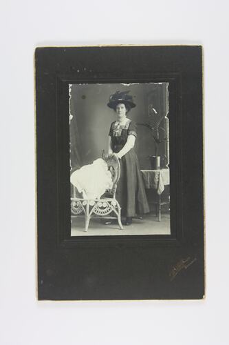 Woman in hat standing next to chair.
