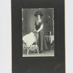 Woman in hat standing next to chair.