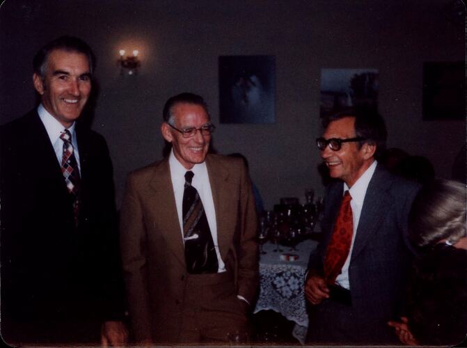 Three men in suits smiling.