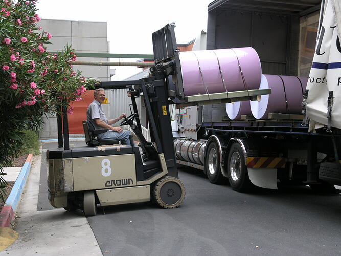 Man on forklift moving large paper roll.
