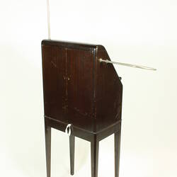 Rear angle view of theremin in wooden case on four legs.