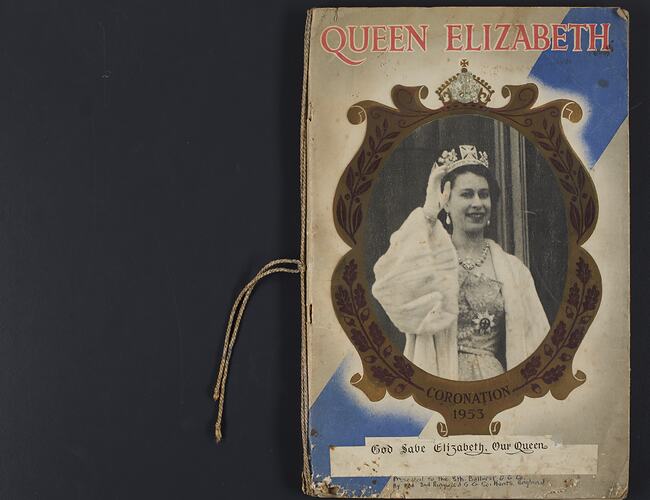 Front cover of scrapbook, black and white image of Queen Elizabeth II pasted over central oval medallion.