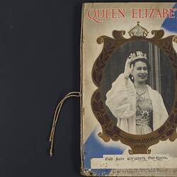 Front cover of scrapbook, black and white image of Queen Elizabeth II pasted over central oval medallion.