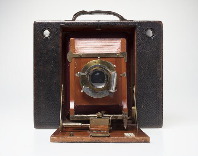 Brown leather-covered camera. Fold out wooden centre, red leather bellows behind lens.