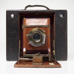 Brown leather-covered camera. Fold out wooden centre, red leather bellows behind lens.