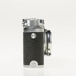 Black camera with metal trim, lens, dials at top corners. Right profile.