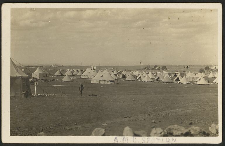 Army camp in a flat outdoor treeless area. Numerous off-white army tents.
