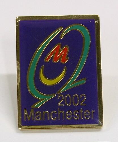 Blue rectangular enamel badge with green, red, yellow logo. Gold lettering.