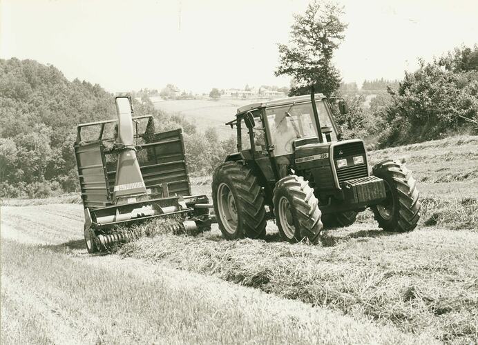 Man driving a tractor towing a PTO forage harvester in field.
