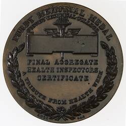 Round medal with central text. Blank scroll above and wreath around edge.