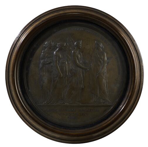 Medal, round, six draped women face woman holding palm. Engraved text. Housed in round wood frame with glass.