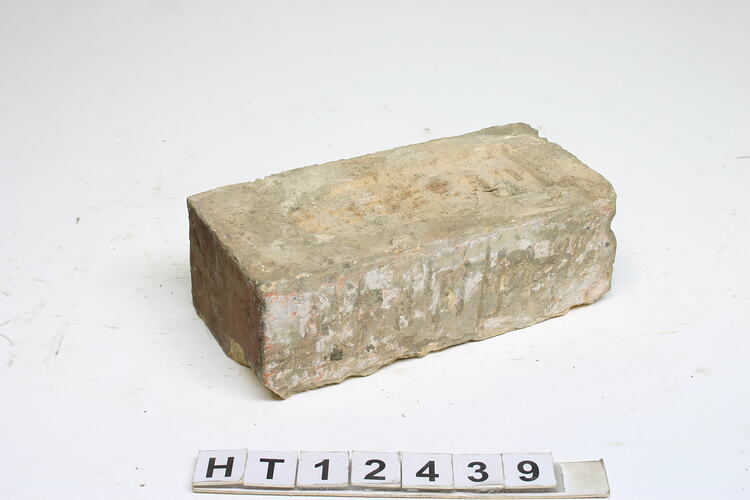 Grey covering worn red, machine pressed brick with a frog on one side.