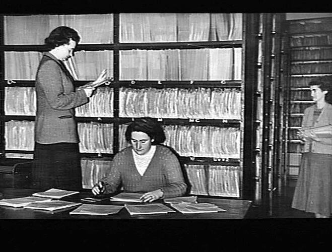 "WORK IN THE FILING ROOM KEEPS THESE THREE YOUNG LADIES BUSY - LEFT TO RIGHT: THE MISSES BETTY SNAITH, EDNA RIGBY AND DOREEN MCKENNA... `SUNSHINE REVIEW': JULY 1950"
