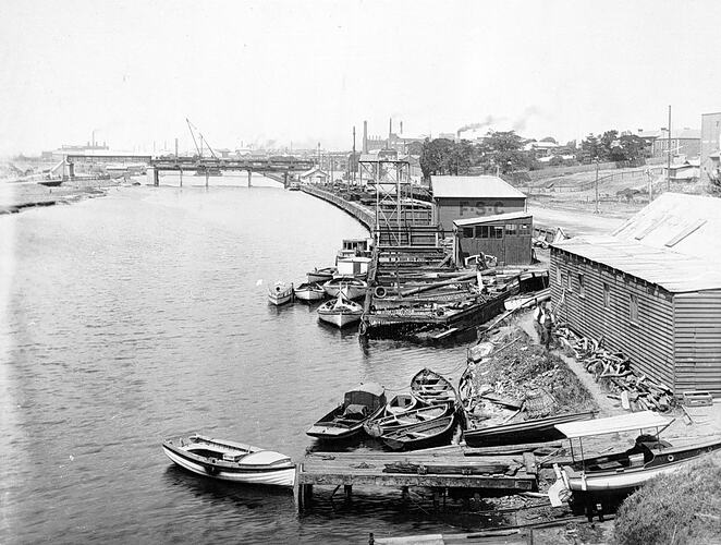 [Boatsheds and jetties on the Maribyrnong River, Footscray, 1930s. The Hopetoun Bridge is in the background.]