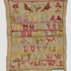 Back of embroidered sampler of coloured alphabet on a woven cream fabric ground. Birds and flowers at top.