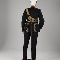 Back of navy officer's uniform with gold at cuff, sash, epaulettes, belt. Red/gold collar. White helmet.