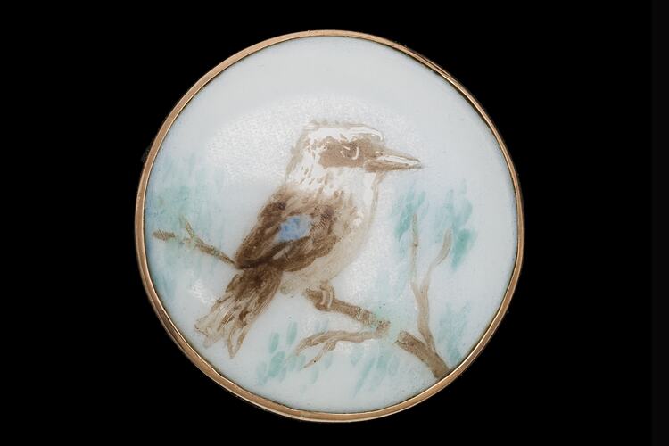 Round white porcelain brooch with hand painted kookaburra in a tree facing right.