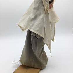 A doll dressed as a nun in a grey dress and white veil