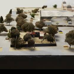 Model detail, building with Australian flag, surrounded by trees. Carpark around it. Mirror building behind.