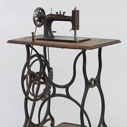 Sewing machine fitted to a metal frame with a wooden bench.
