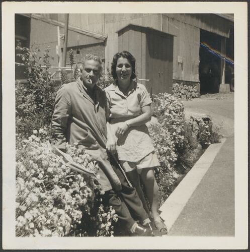 Man and woman posing outside against a garden bed.