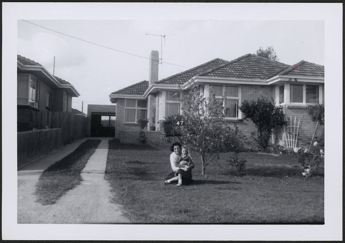 Woman and young child in front garden of brick house.