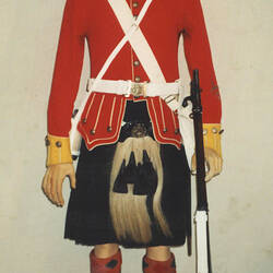 Military uniform on mannequin with red jacket, tartan kilt and sporran and cap, holding a rifle,