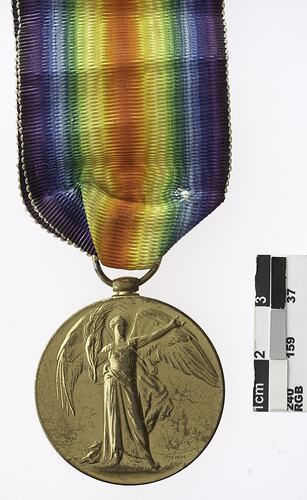 Round gold coloured medal with winged woman and rainbow ribbon attached.