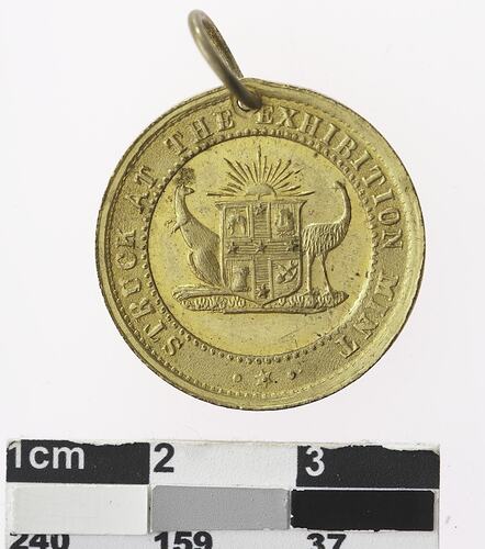 Round gold coloured medal with coat of arms and text surrounding.
