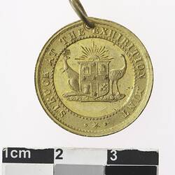 Round gold coloured medal with coat of arms and text surrounding.