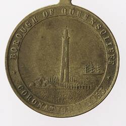 Round silver coloured medal with lighthouse and text surrounding.