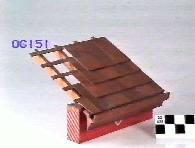 Slate laying model. Section of eaves supported by brackets and fascia board. Has brown slate tiles.