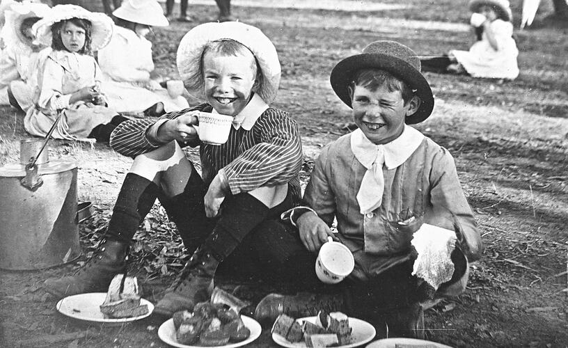 Two young boys sitting on ground having afternoon tea.