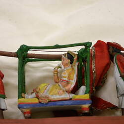 Three colourful dolls with two carrying a girl in a palanquin.
