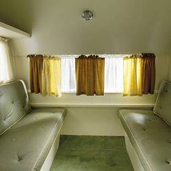 Caravan cream internal view, twin grey green couch, yellow and white curtains.