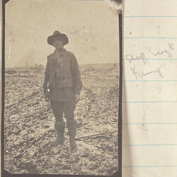 Soldier with slouch hat standing in a snow covered field, tents in background.
