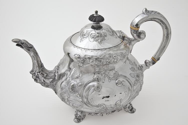Ornate silver teapot with lid. Left profile.