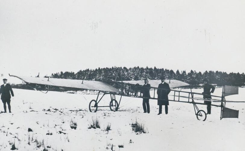 Four men standing next to monoplane in snow covered ground.