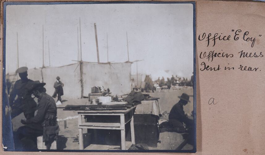 Servicemen in camp with tent, tables and boxes.