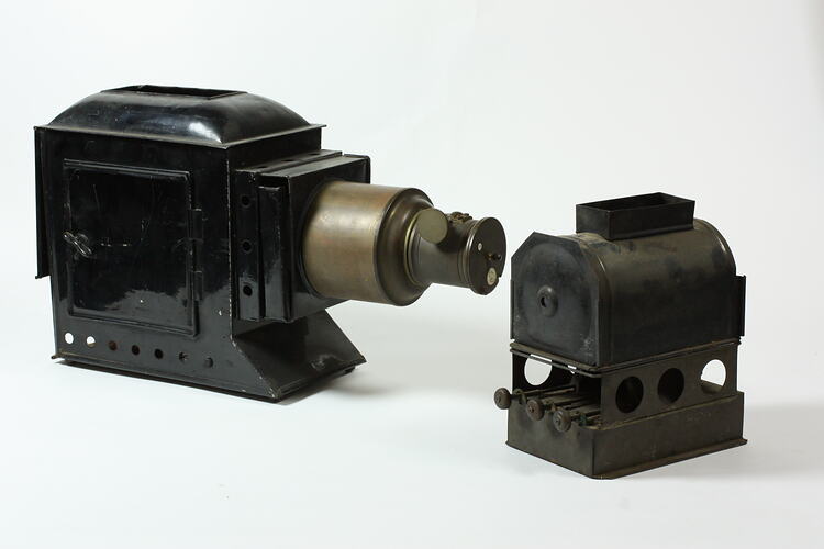 Black metal magic lantern projector with brass lens and separate cube shaped three wick lamp burner.