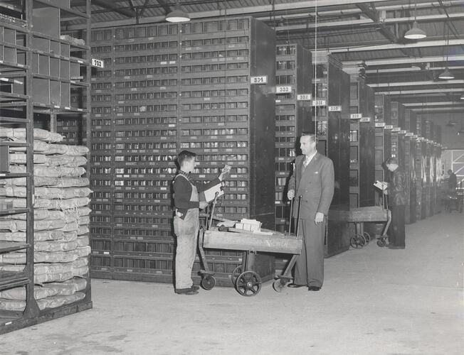 3 men standing in front of shelving racks.