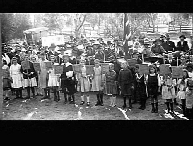 Crowd of people, row of children in front holding signs.