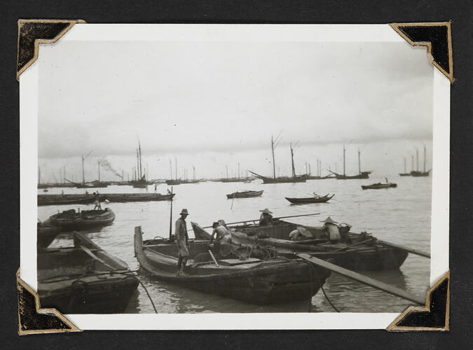 Men on two boats in harbour, other boats in background.