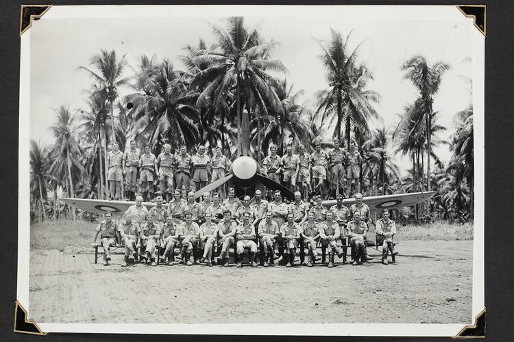 Group portrait of three rows of men, with back row standing on wings of aeroplane.